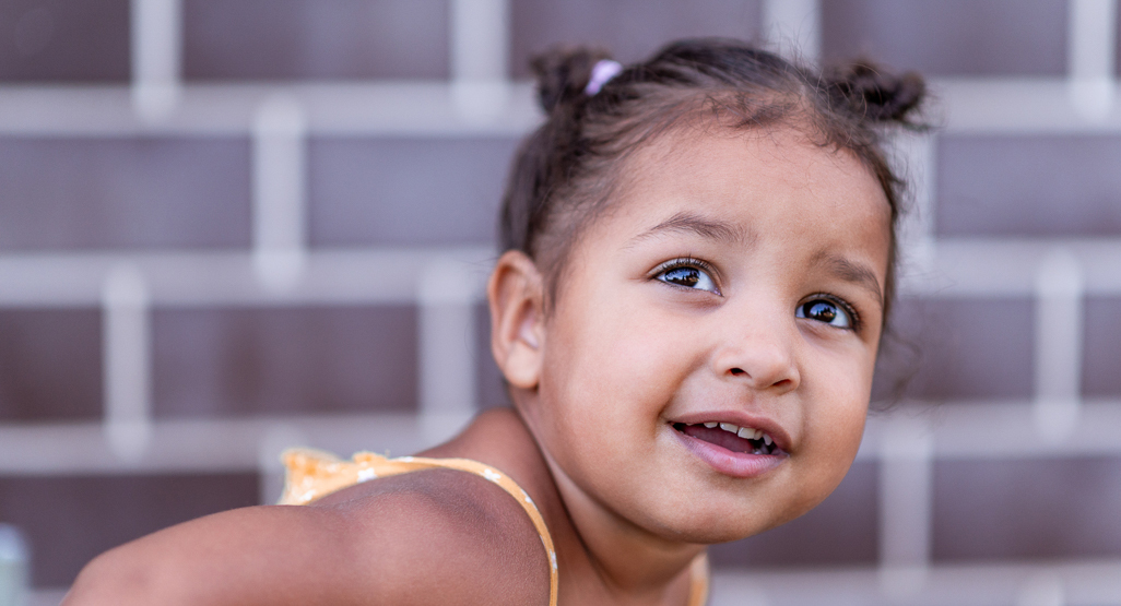 close up of smiling little girl in front of brick wall