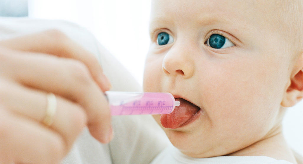 baby getting oral medicine through plastic syringe