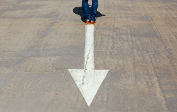 male person standing at the end of a painted arrow on the road
