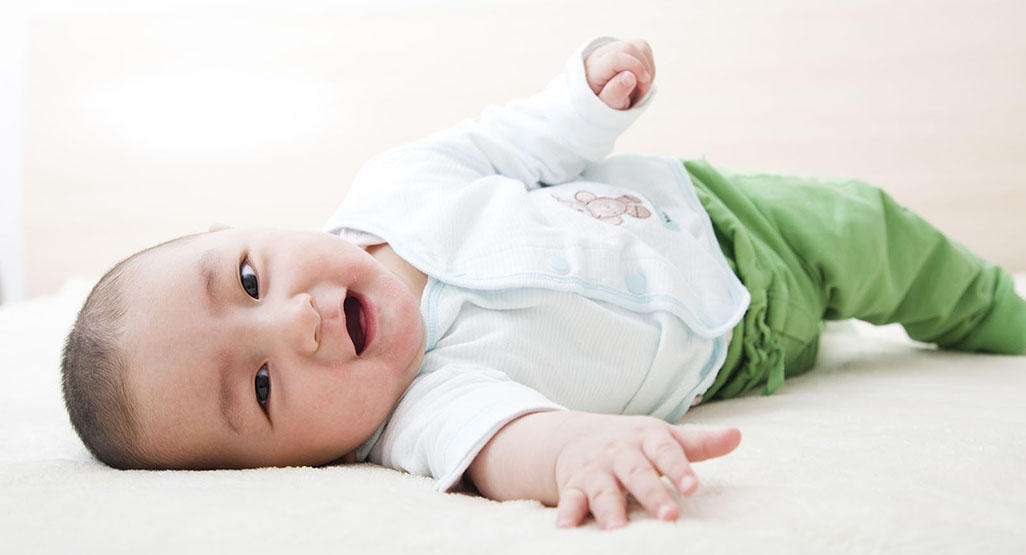smiling baby on blanket trying to roll over