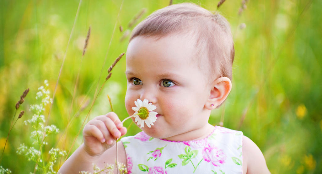 baby in a field smelling flower