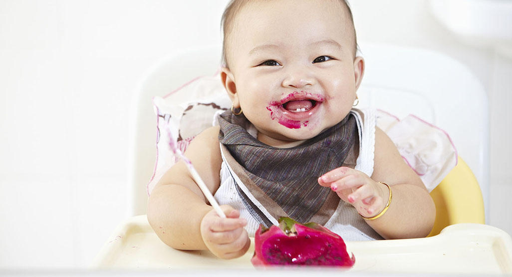 baby eating in a high chair with food all over her face