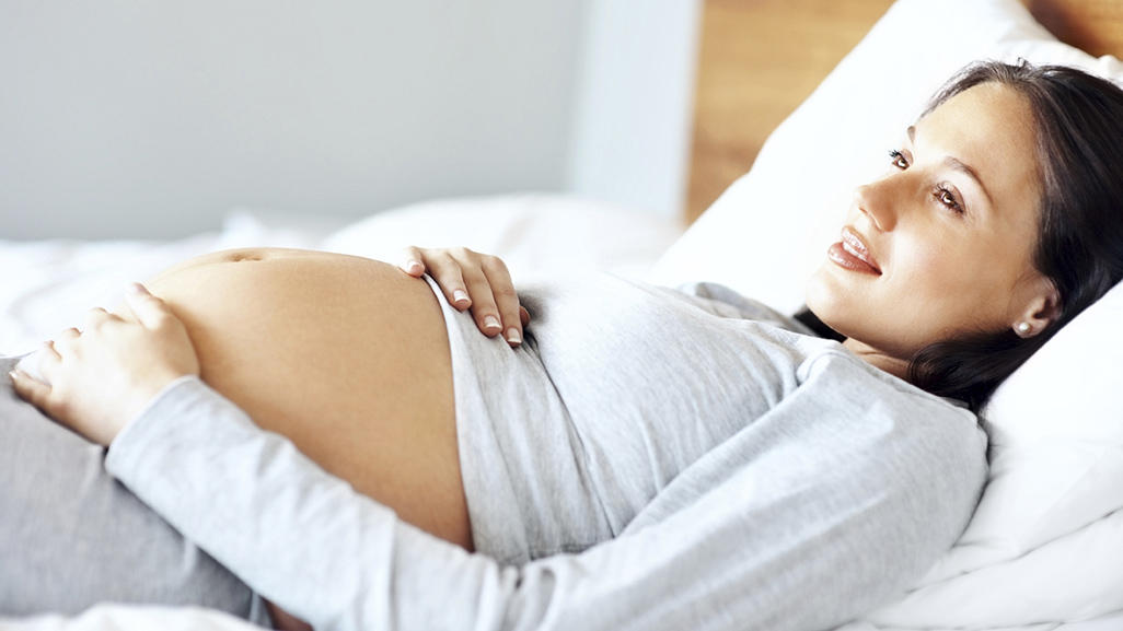 pregnant woman laying in bed with pregnant belly exposed