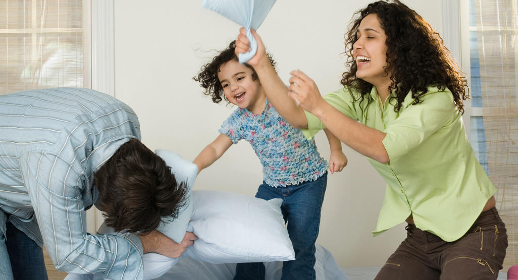 mom dad and child having a pillow fight