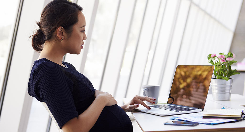 pregnant woman sitting at desk working on laptop
