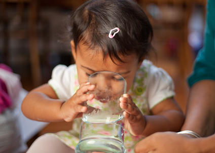 little girl drinking water from a big glass