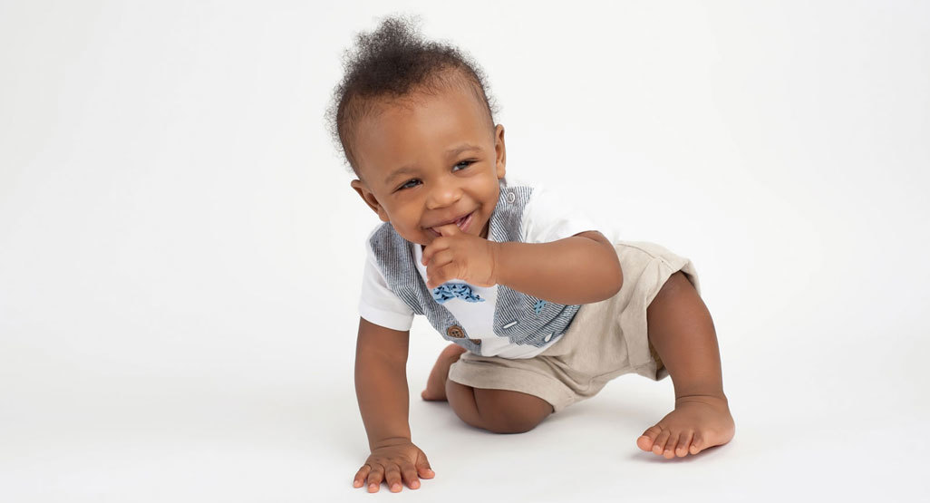 A fashionably dressed baby smiles from a squatting position