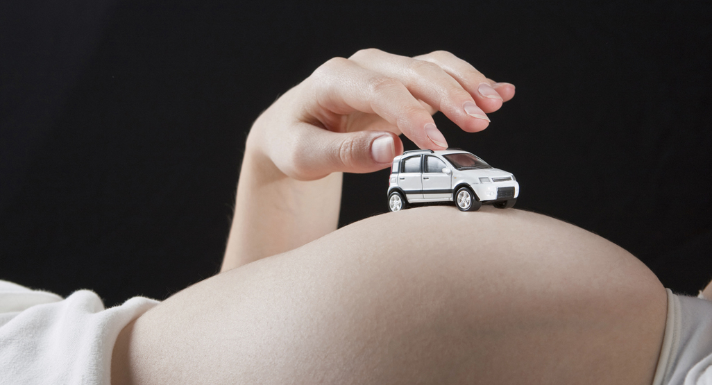 A woman rolls a toy car over her pregnant belly