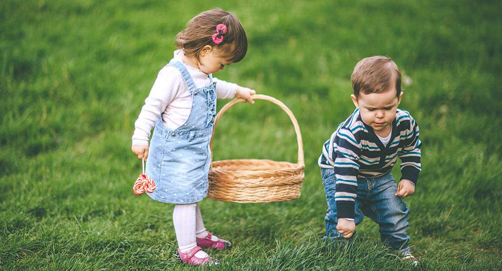 little girl holding a basket while little boy picks grass