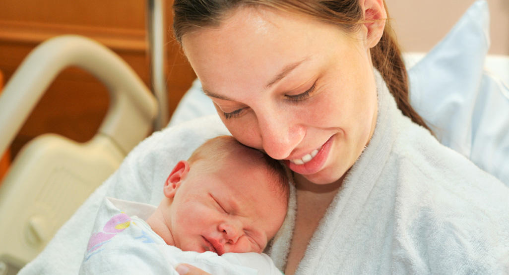 smiling woman holding a newborn in hospital bed