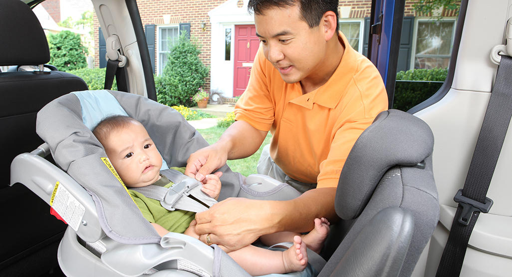 child lying in baby car seat while man trying to put a seatbelt on