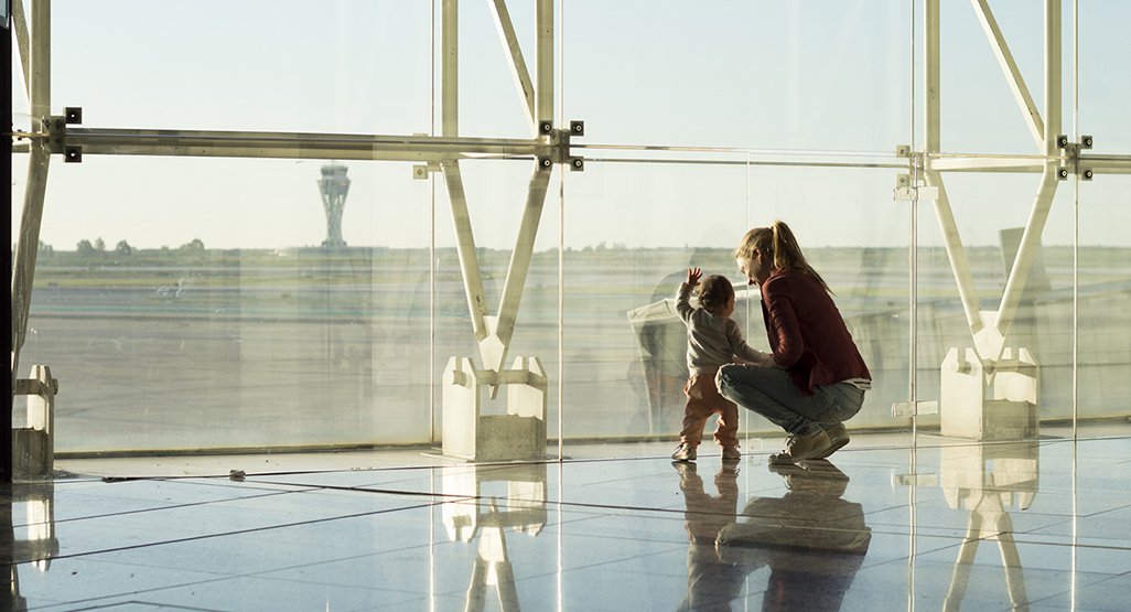 mother and child standing in front of a large window looking out at planes