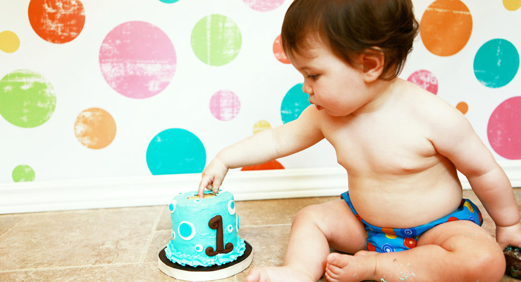 a year old baby sitting on a floor and digging his finger into the top of a small blue birthday cake