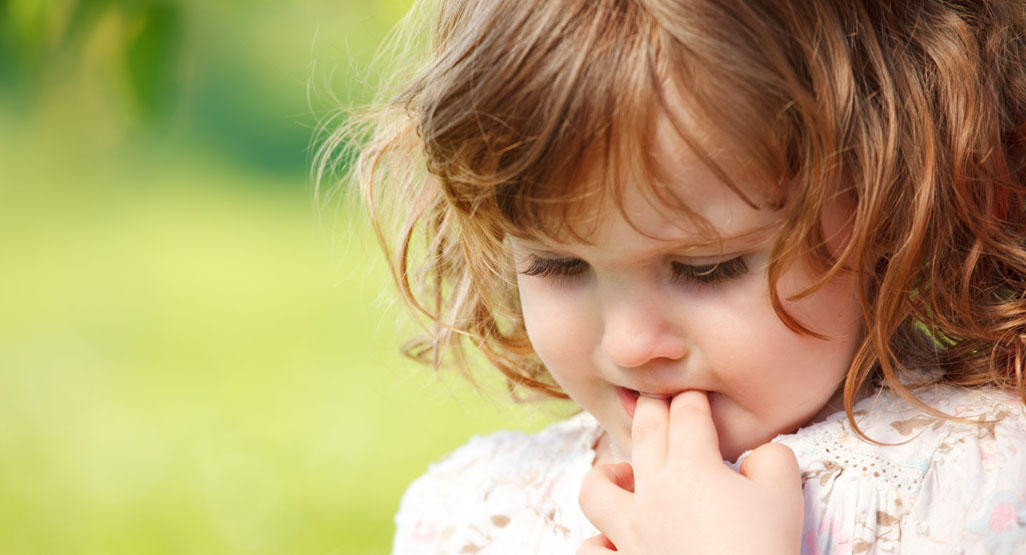 little girl biting two fingers, looking at the ground