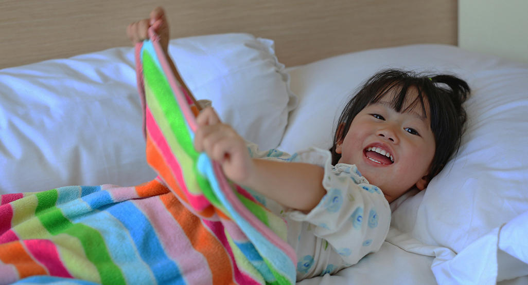 asian girl lying on the bed wrapped up in a colorful striped blanket