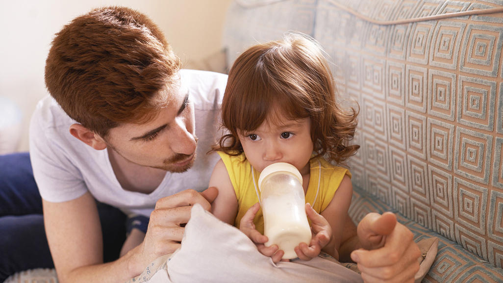 child in a dad's hug drinking milk from a baby bottle
