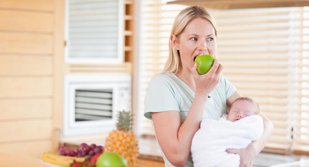 woman holding a baby in her left arm and eating apple with her right hand