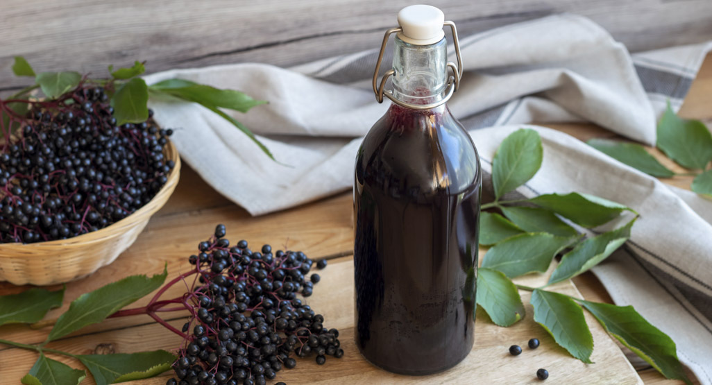 bottle of elderberry syrup surrounded by elderberries and leaves