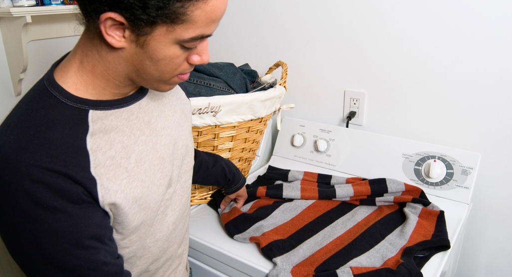 man folding a sweater on a washing machine