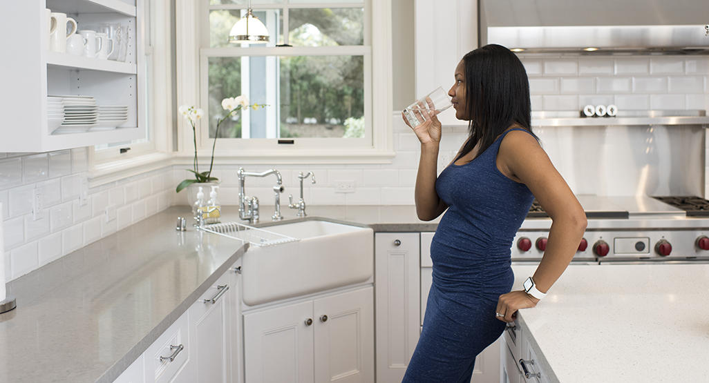 pregnant woman leaning on the kitchen counter and drinking water