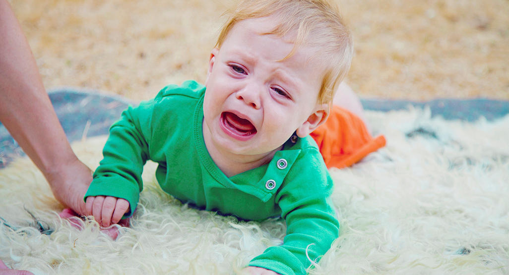 the baby is attempting to crawl on the furry carpet, but is crying instead