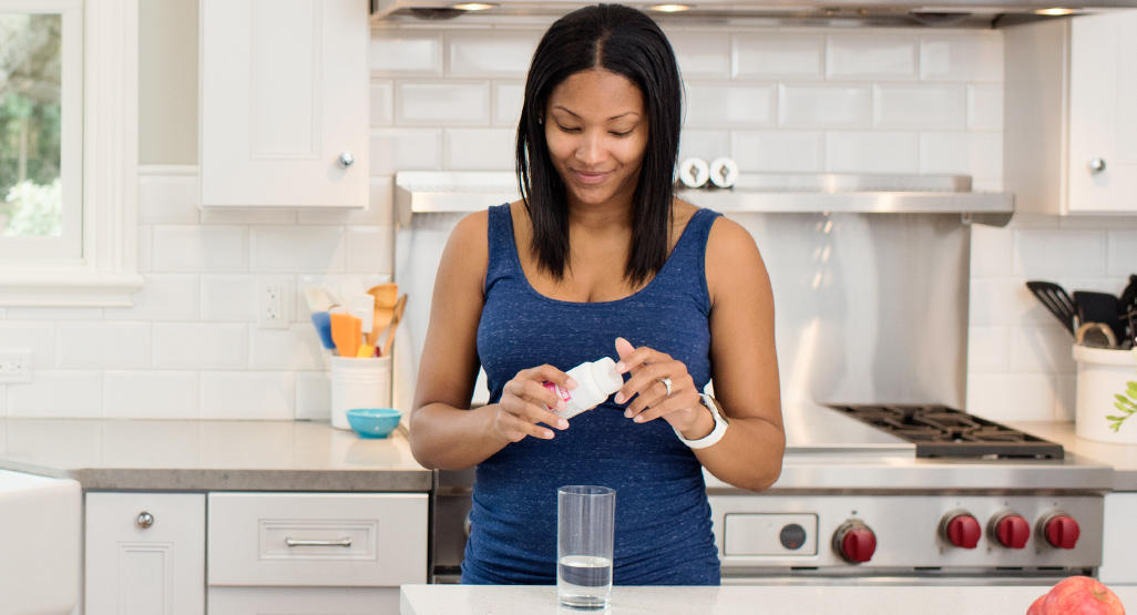 woman standing in the kitchen and taking pills