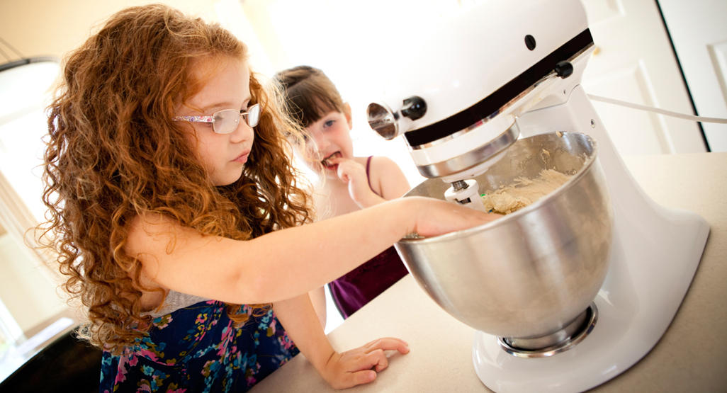 girl kneading dough in a mixer with her sister
