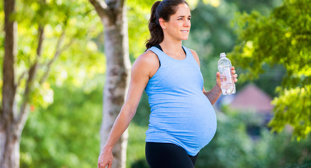 pregnant woman walking outdoors, holding a bottle of water