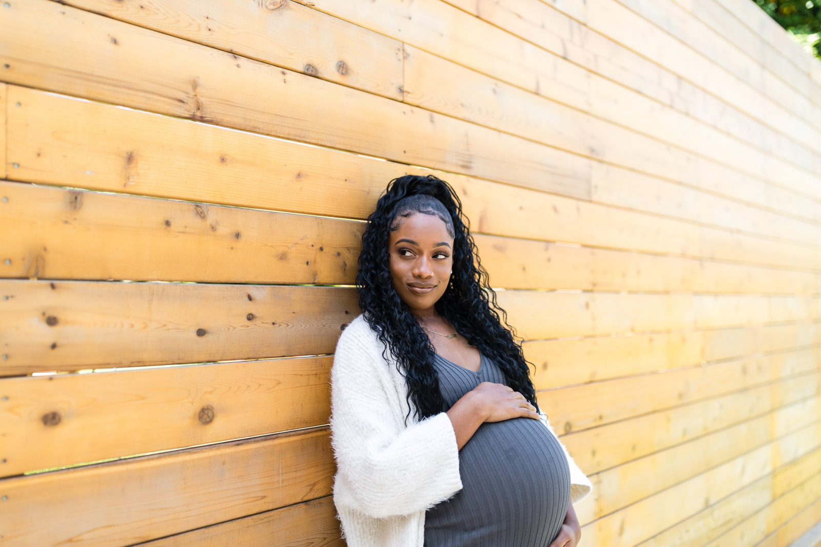 Black, pregnant woman with long hair leaning against a fence.