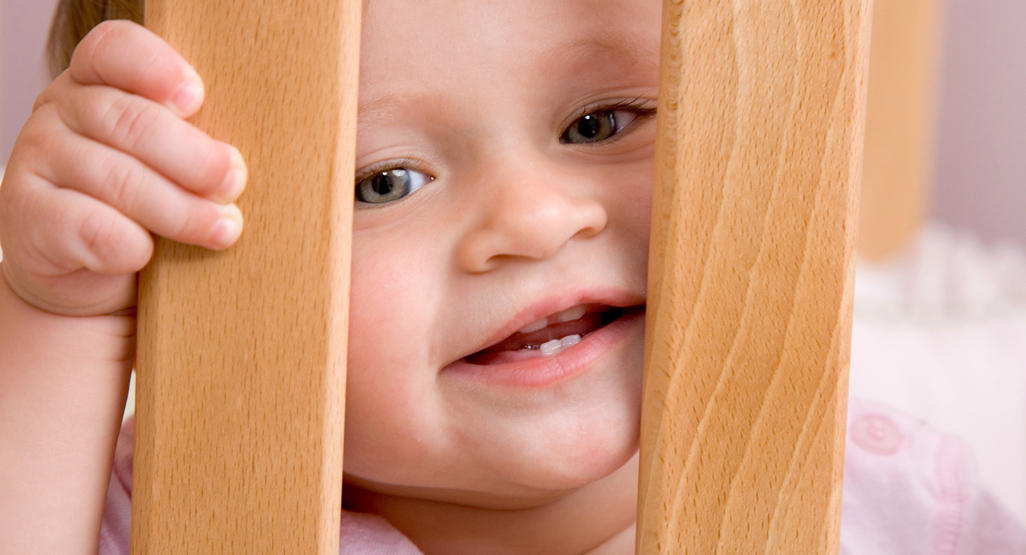 baby looking through wooden crib