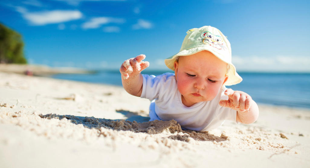 baby girl wearing sun hat playing on sandy beach