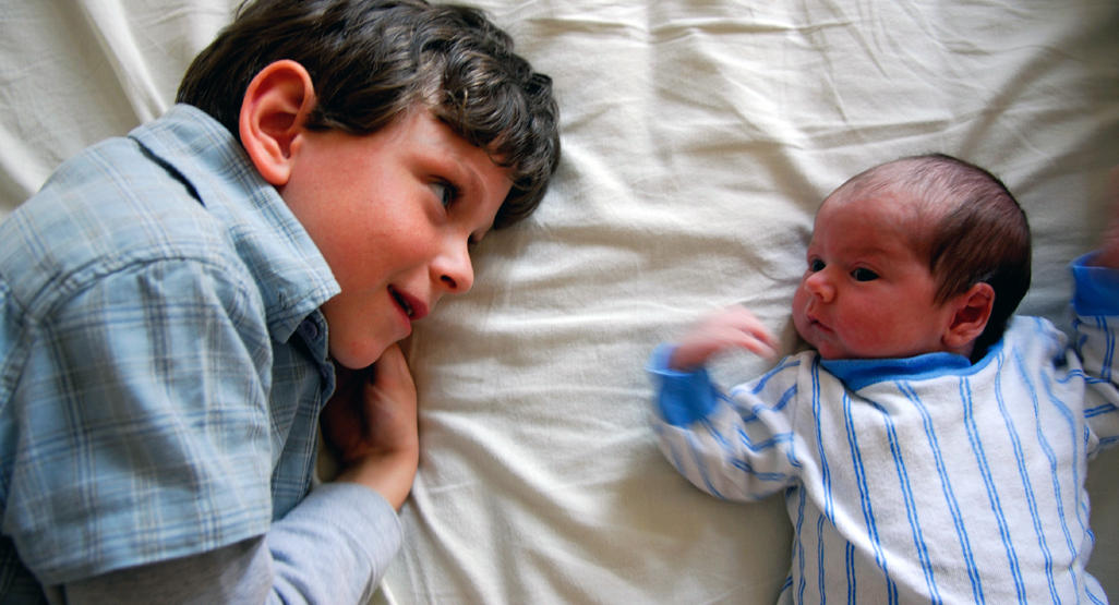 boy watching a newborn sibling while both lying on a bed