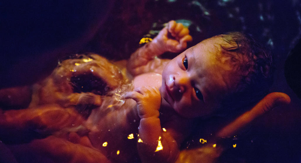 newborn being held in a water birth bath