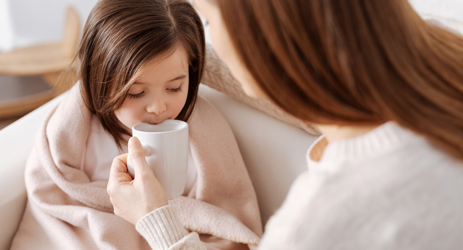 mother holding a mug while a seemingly under the weather child drinks from it