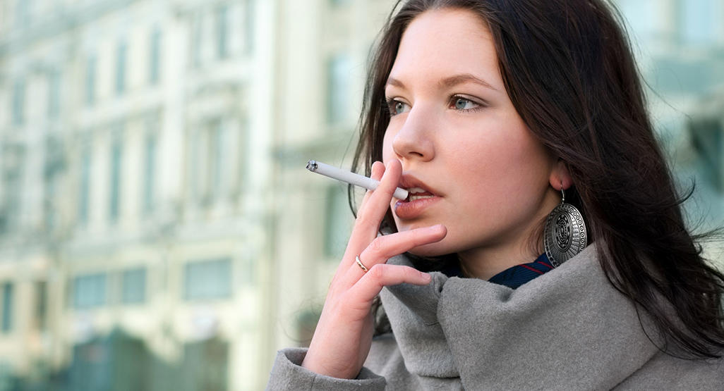 woman with green eyes and brown straight hair is smoking a cigarette
