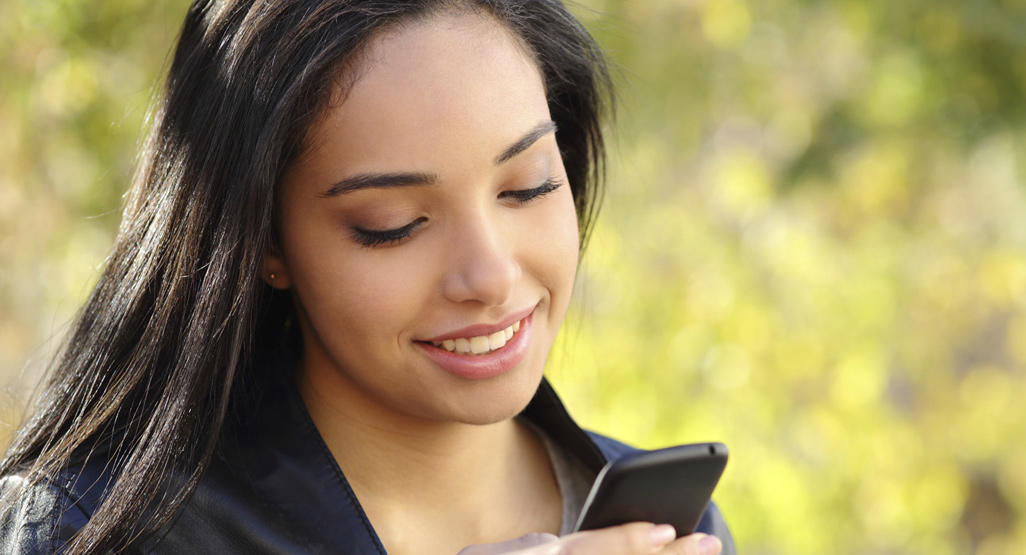 woman smiling while looking at her mobile phone