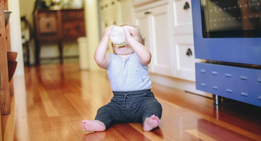 A baby drinks from a bottle while sitting in a living room