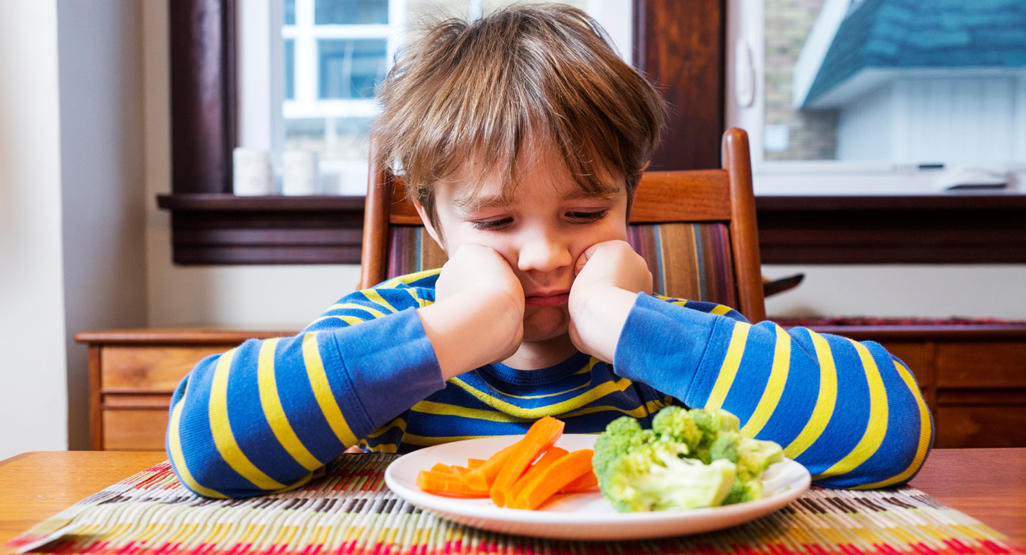 kid looking bored at the carrots and broccoli at his plate