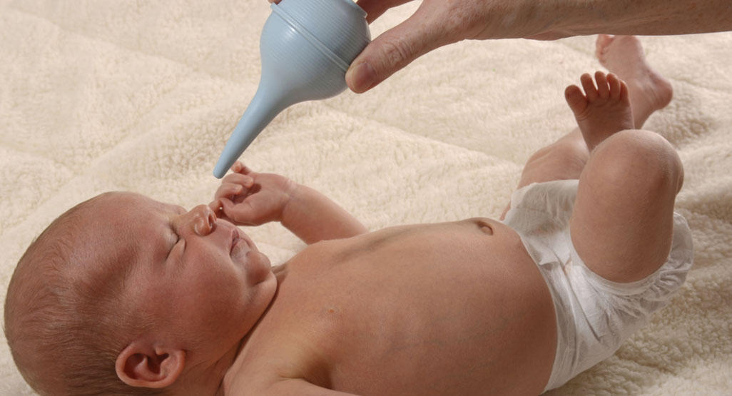 baby having a bulb syringe put into nostril by adult