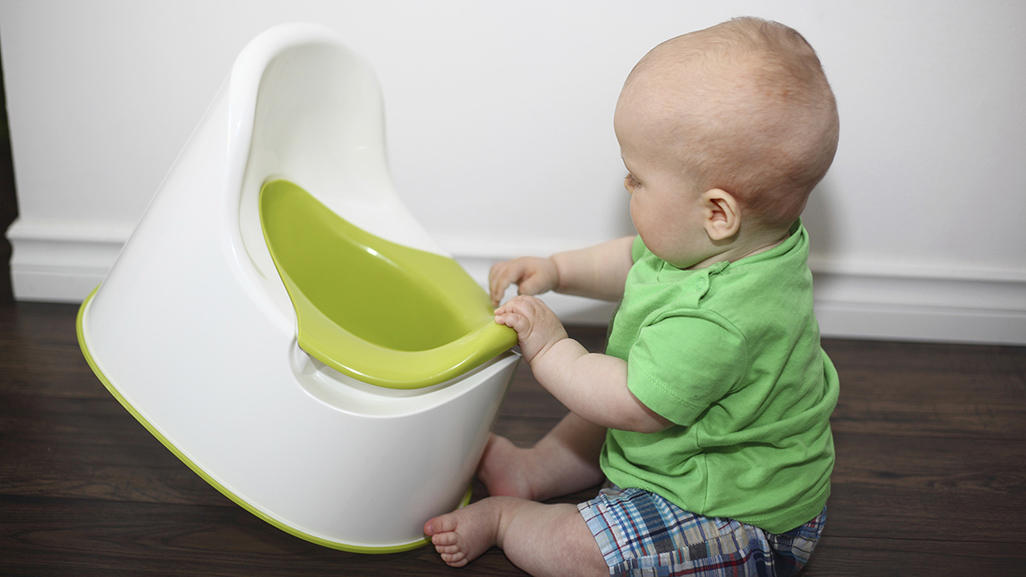 baby sitting on the floor playing with a potty chair