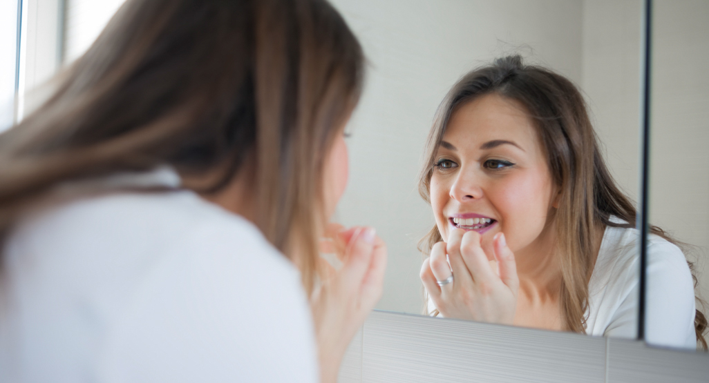 woman looking in a mirror and checking out her teeth