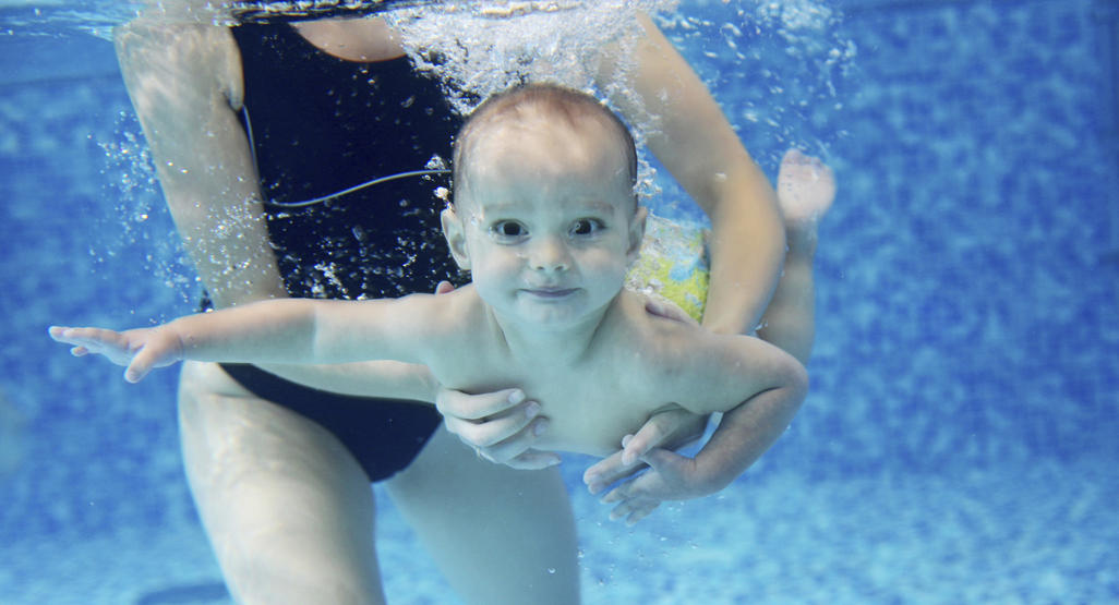mom holding an infant under water while she swims