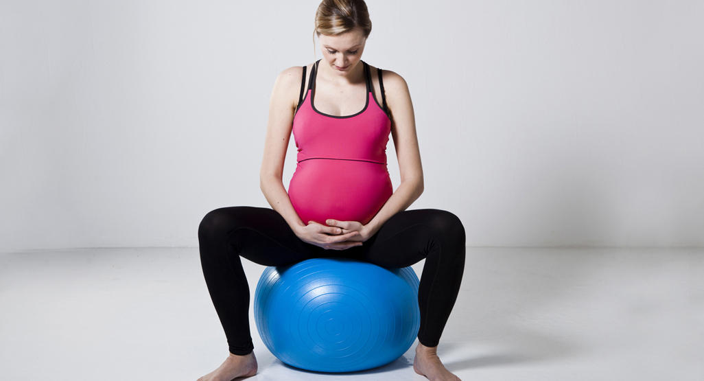 pregnant woman sitting down on a gym ball