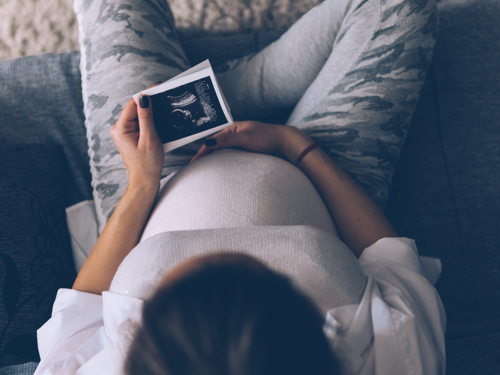 pregnant woman sitting on couch looking at ultrasound photo
