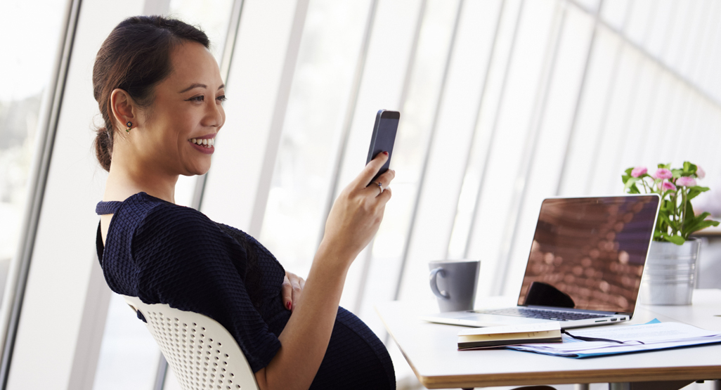 pregnant woman sitting at the desk, looking at her phone and smiling