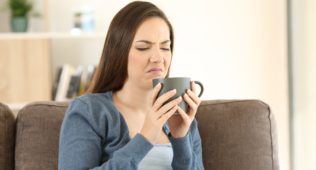 woman smelling a beverage from her cup with disgusted expression on her face