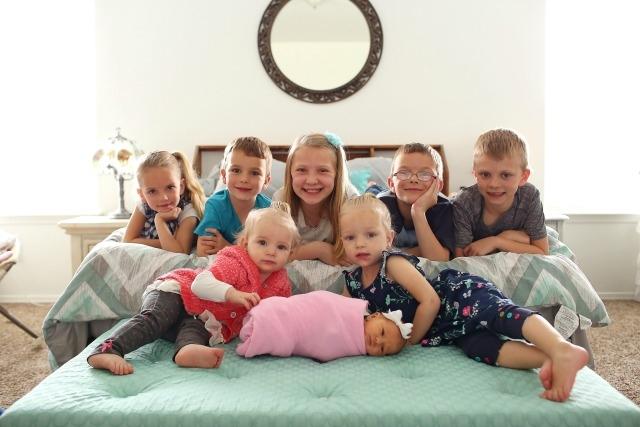 three boys, four girls, and a baby lying on a bed