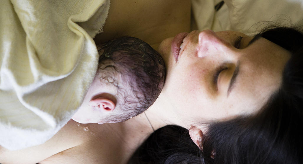 woman sleeping with her newborn which is covered by towel sleeping on her shoulder