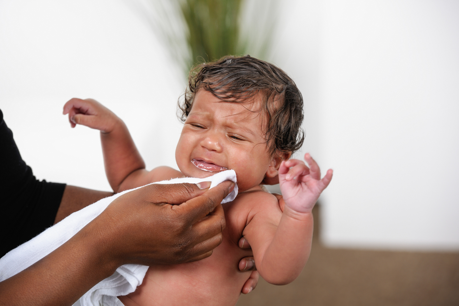 very upset baby having vomit wiped from his face