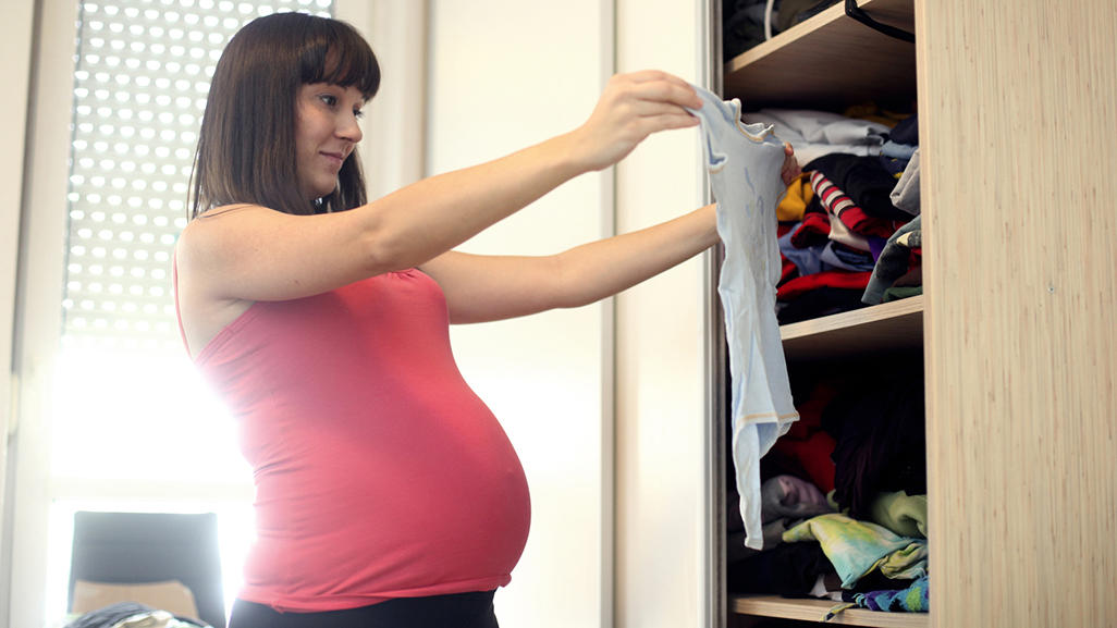 pregnant woman looking at baby clothes in front of an open closet